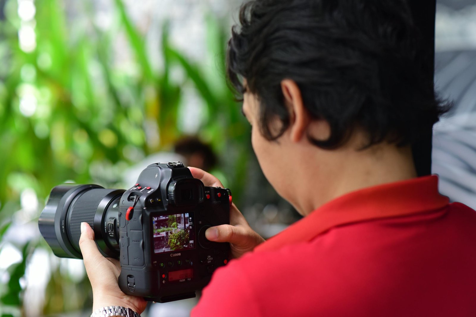 A photographer focuses on capturing nature using a DSLR camera in an indoor setup with green plants