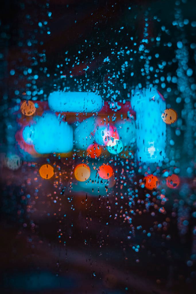 Colorful city lights creating bokeh effect through raindrops on a window.