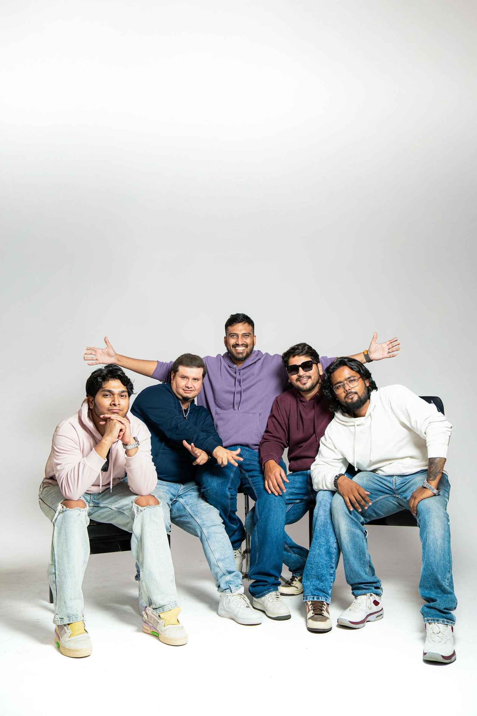 Five friends posing casually in a studio setting, expressing camaraderie with smiles and relaxed postures.