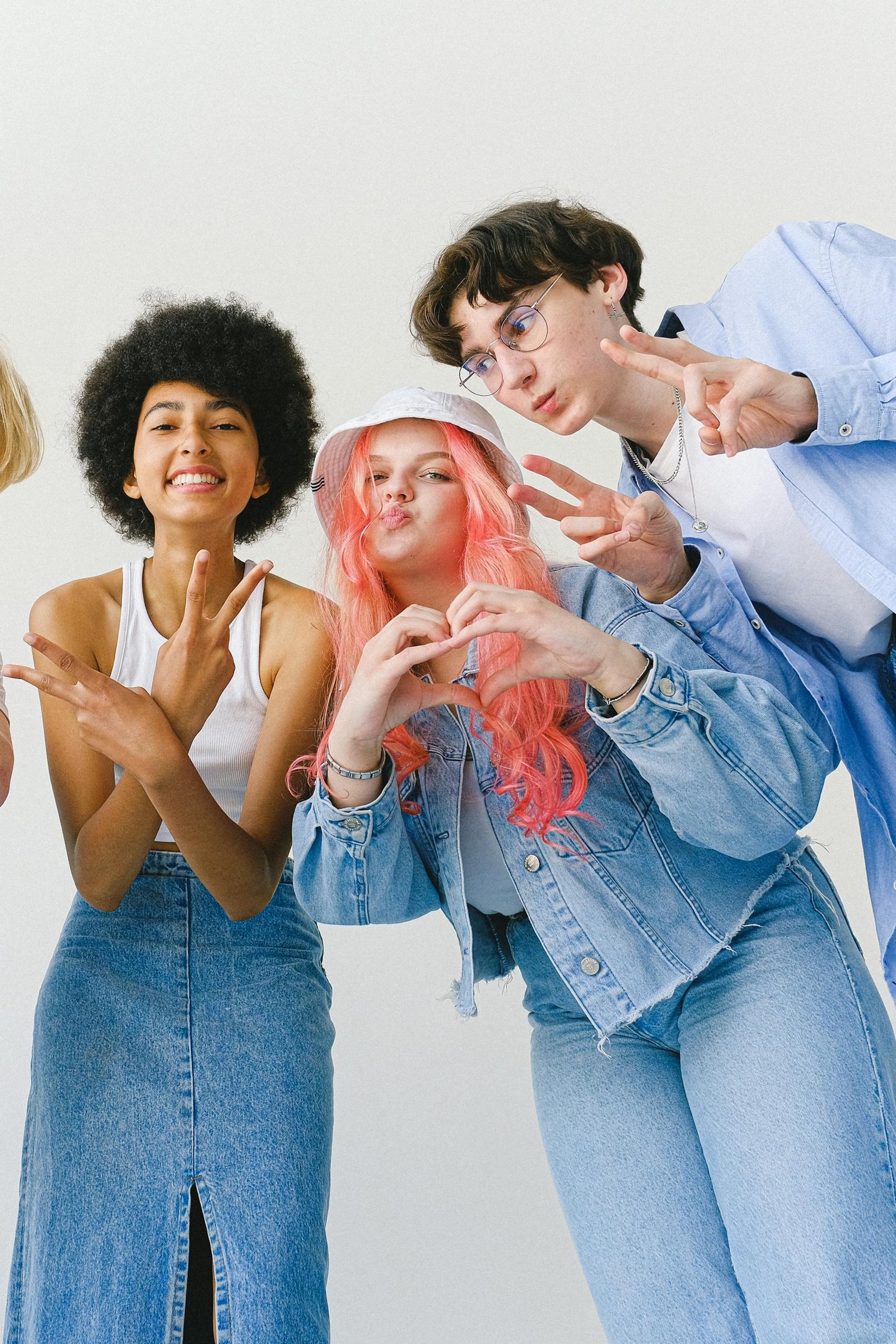 Low-angle view of joyful teenagers in denim, smiling and gesturing towards the camera against a white background